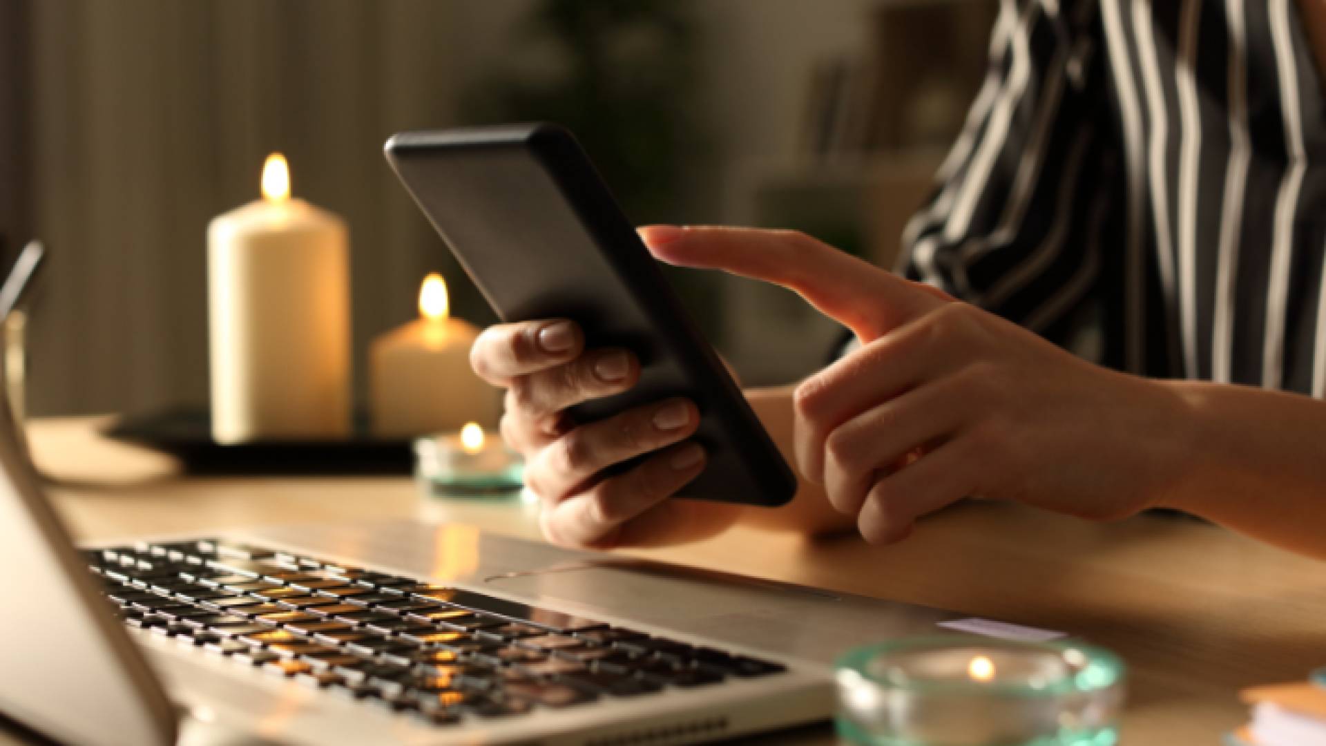 صورة تعبيرية لفتاة تحمل جهازها الخلوي وبجواراها شمعة