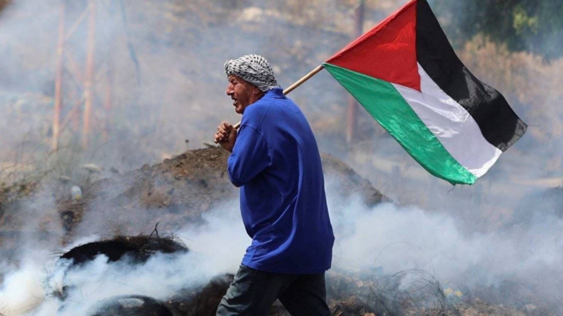 فلسطيني يحمل علم وسط الدخان الصادر عن قنابل الاحتلال