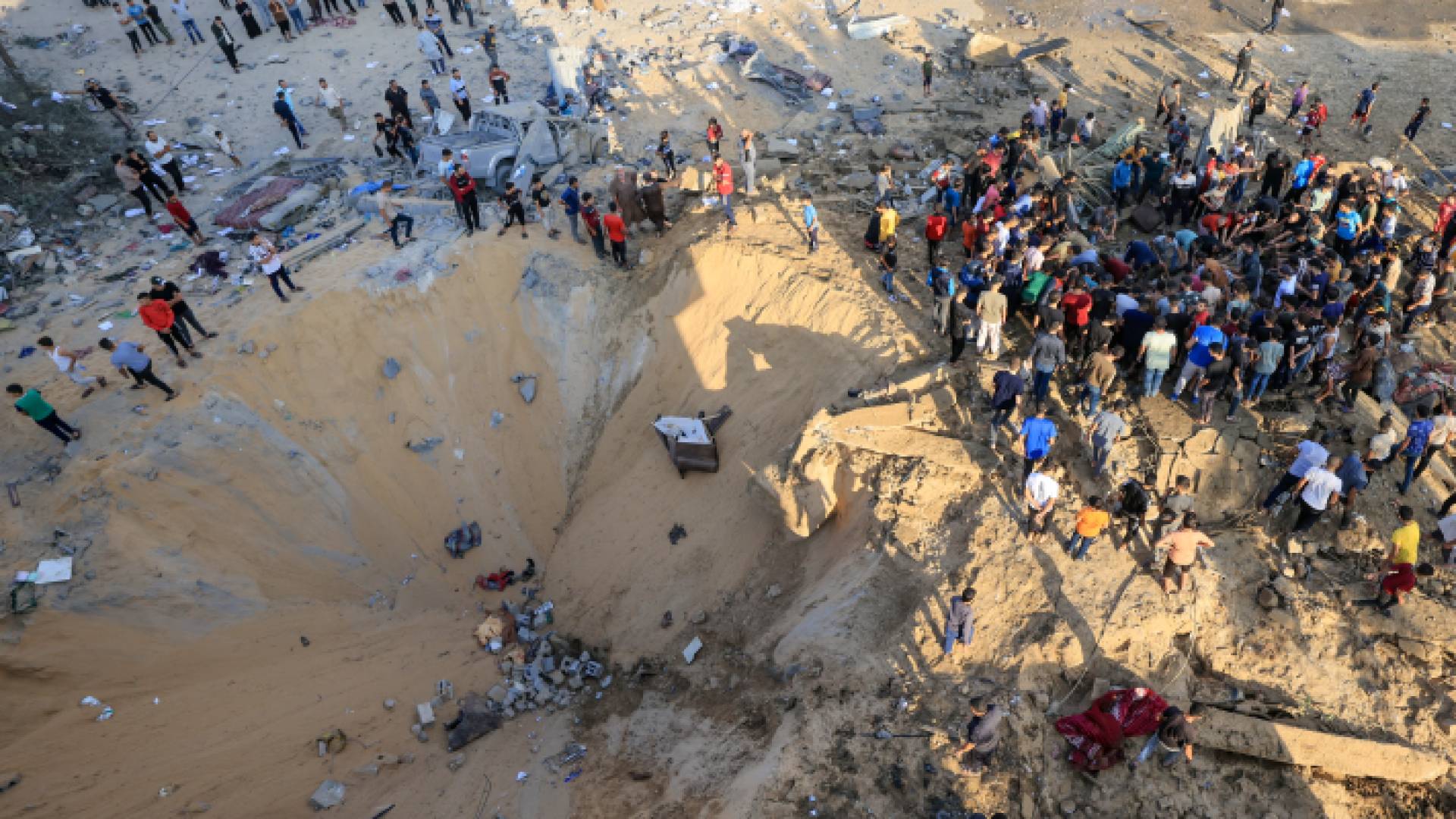 فلسطينيون يقفون بجوار حفرة ناجمة عن انفجار ضربة جوية في خان يونس جنوب قطاع غزة