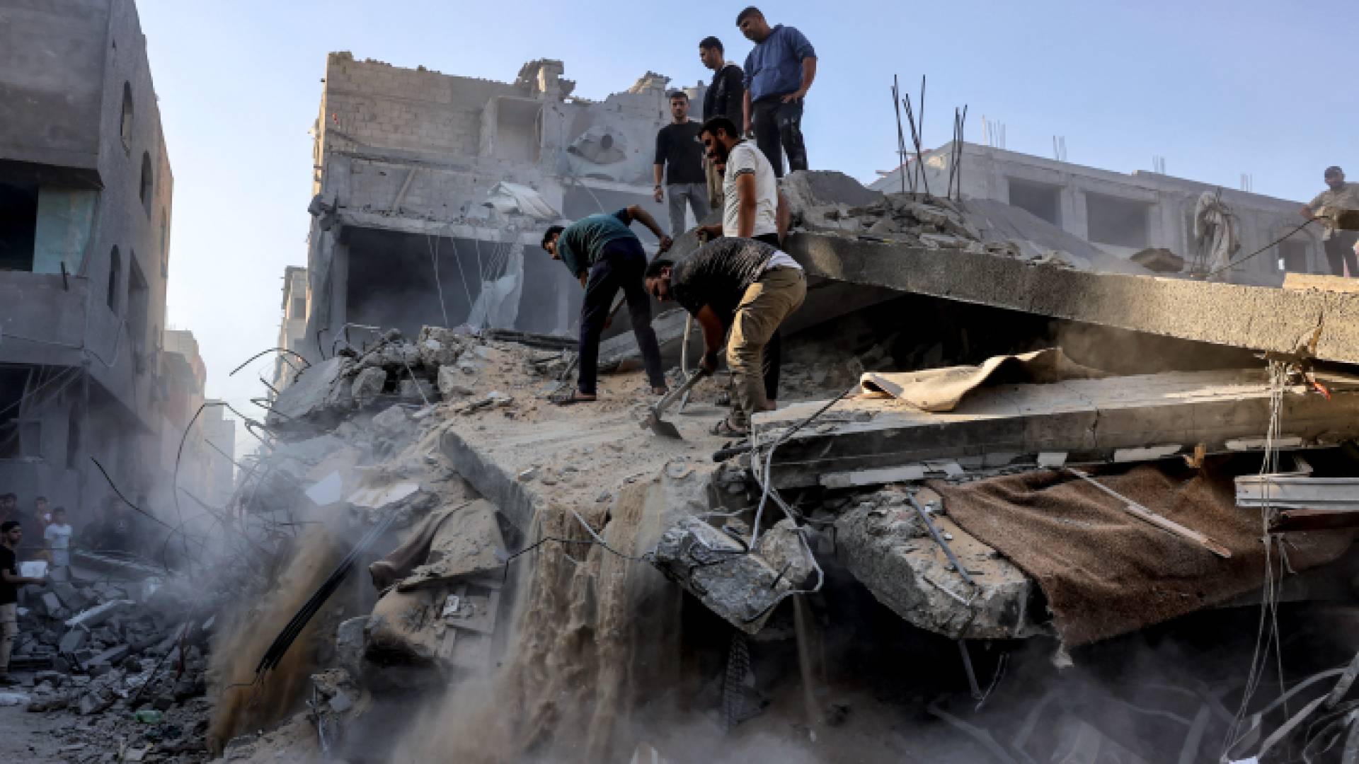 فلسطينيون يقفون فوق أحد المنازل التي تعرضت للدمار في قطاع غزة