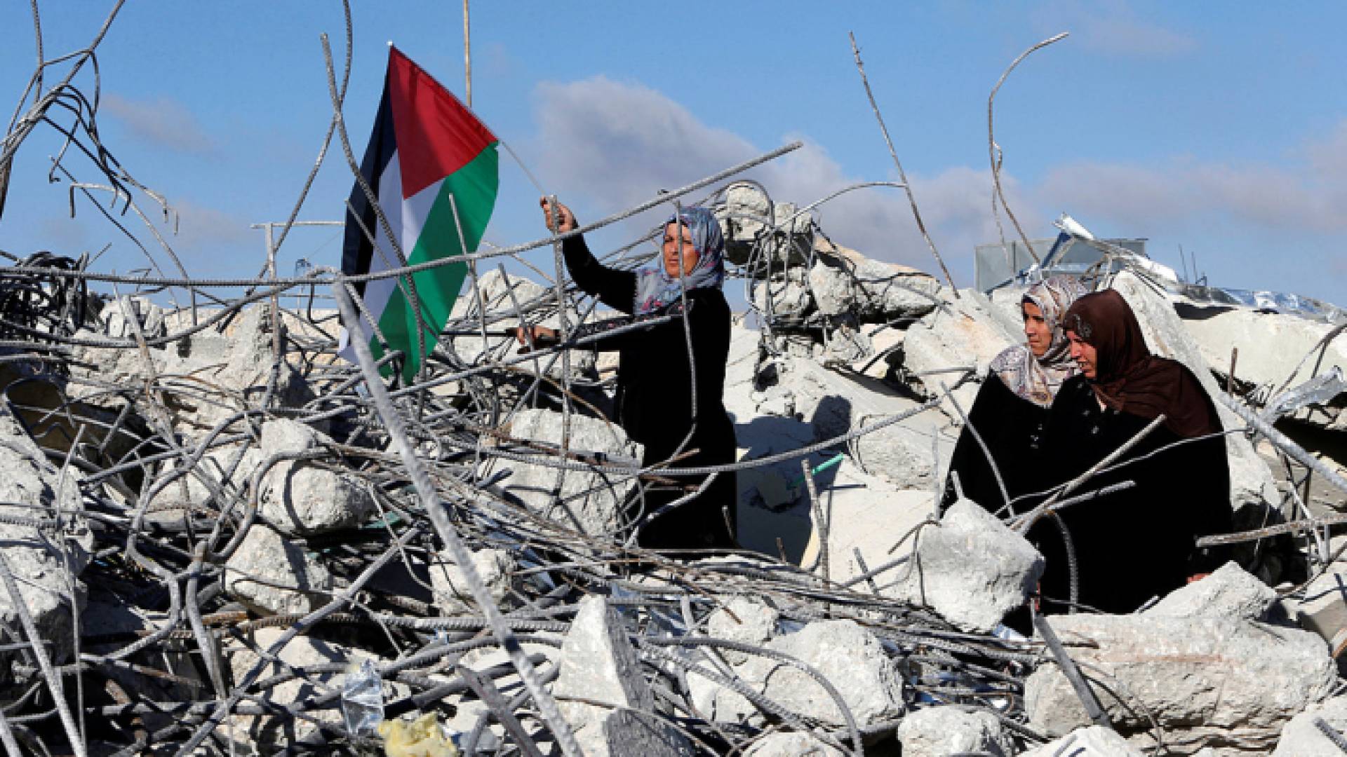 فلسطينية تحمل علم فلسطين فوق الركام