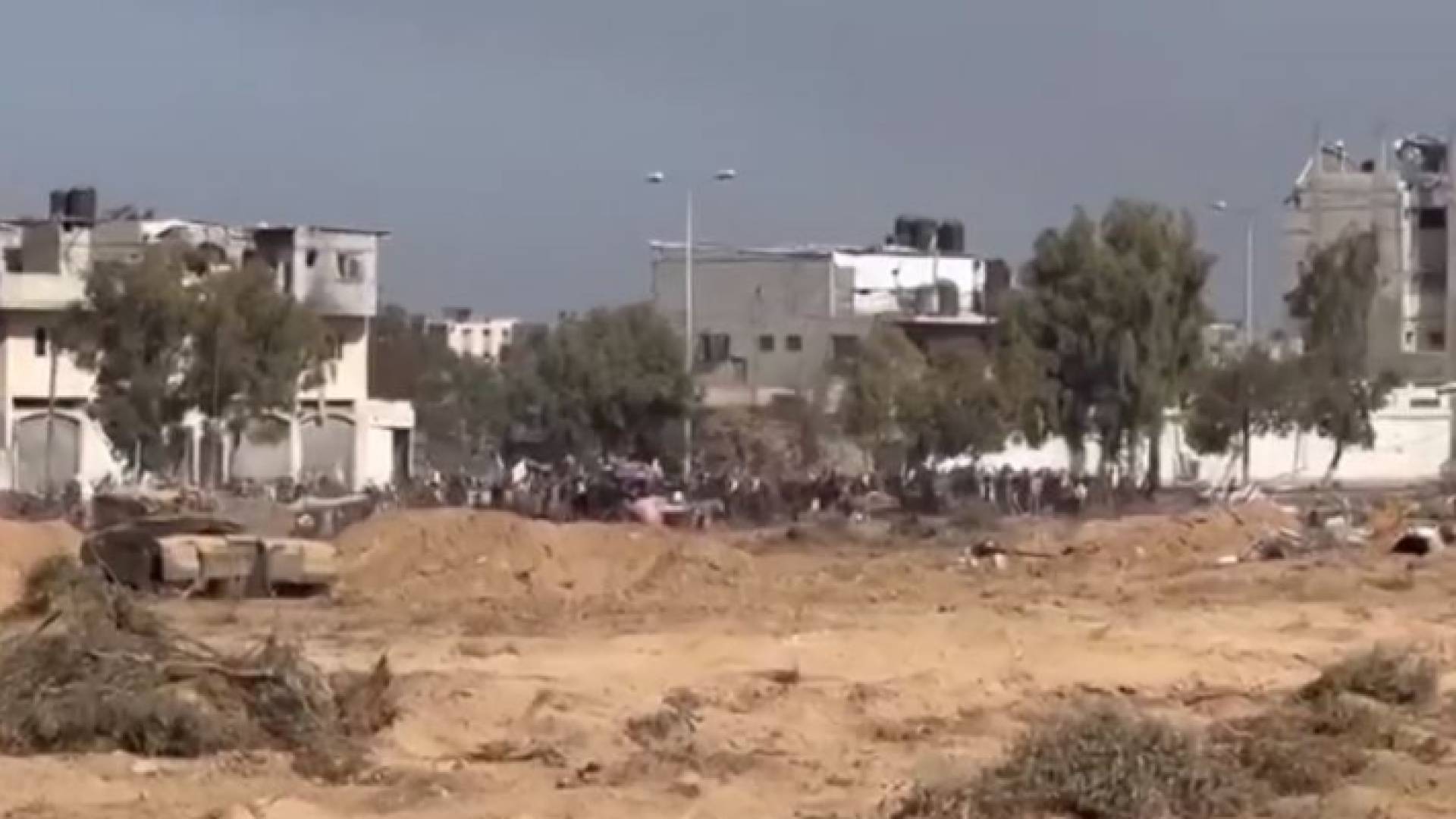 صورة ملتقطة من مقطع الفيديو الذي نشره الاحتلال الإسرائيلي تظهر دبابة مقابل توافد فلسطينيين نازحين بالرايات البيضاء