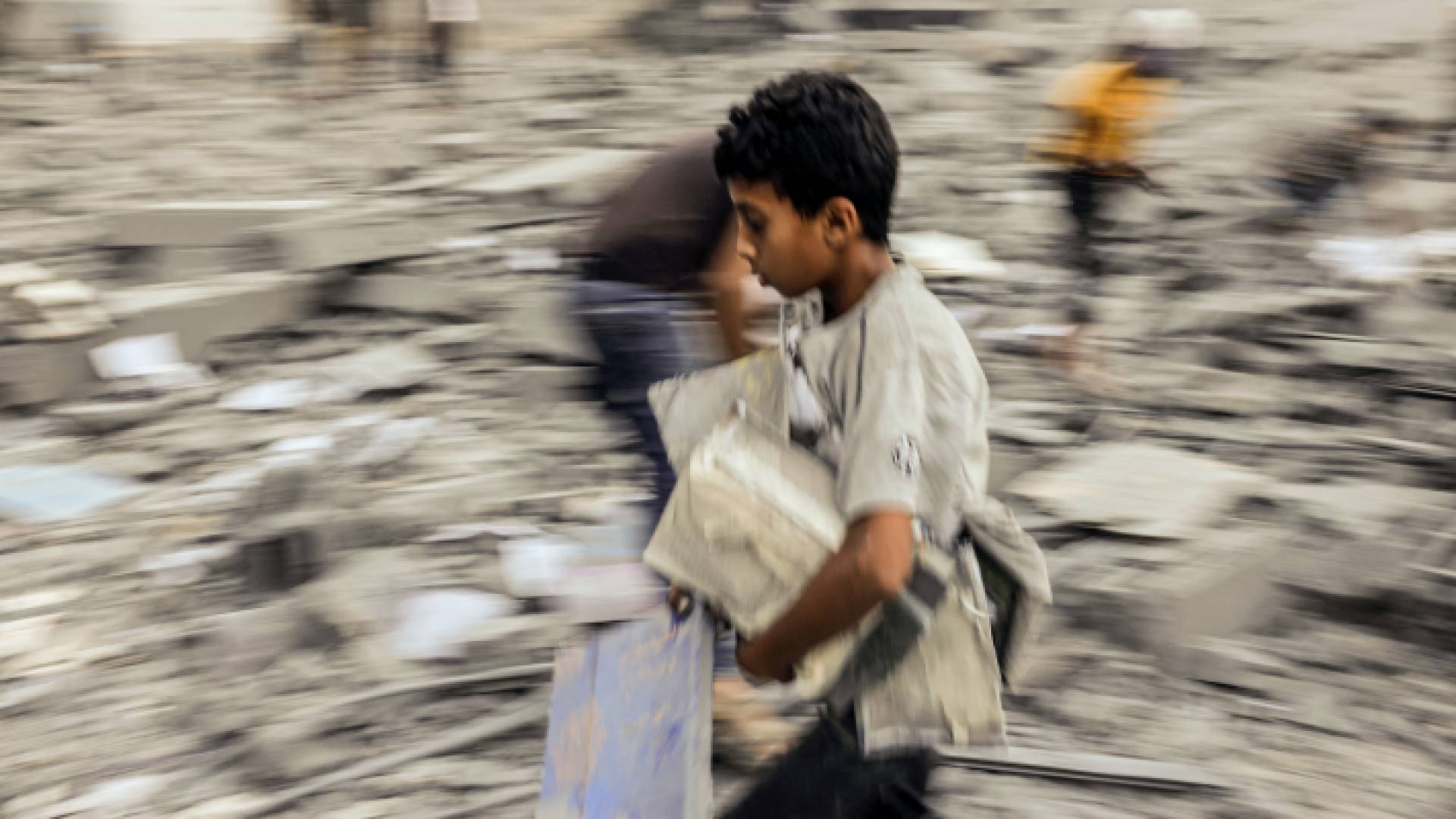طفل من غزة يحمل كتب ويركض هربا من قصف الاحتلال