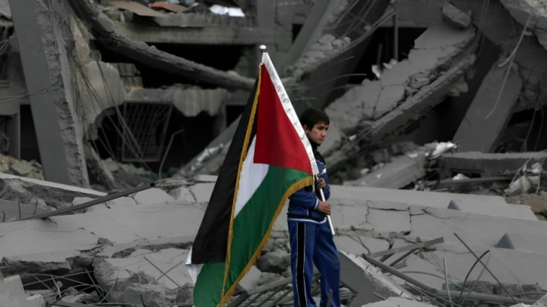 فلسطيني يرفع علم دولة فلسطين بين الركام