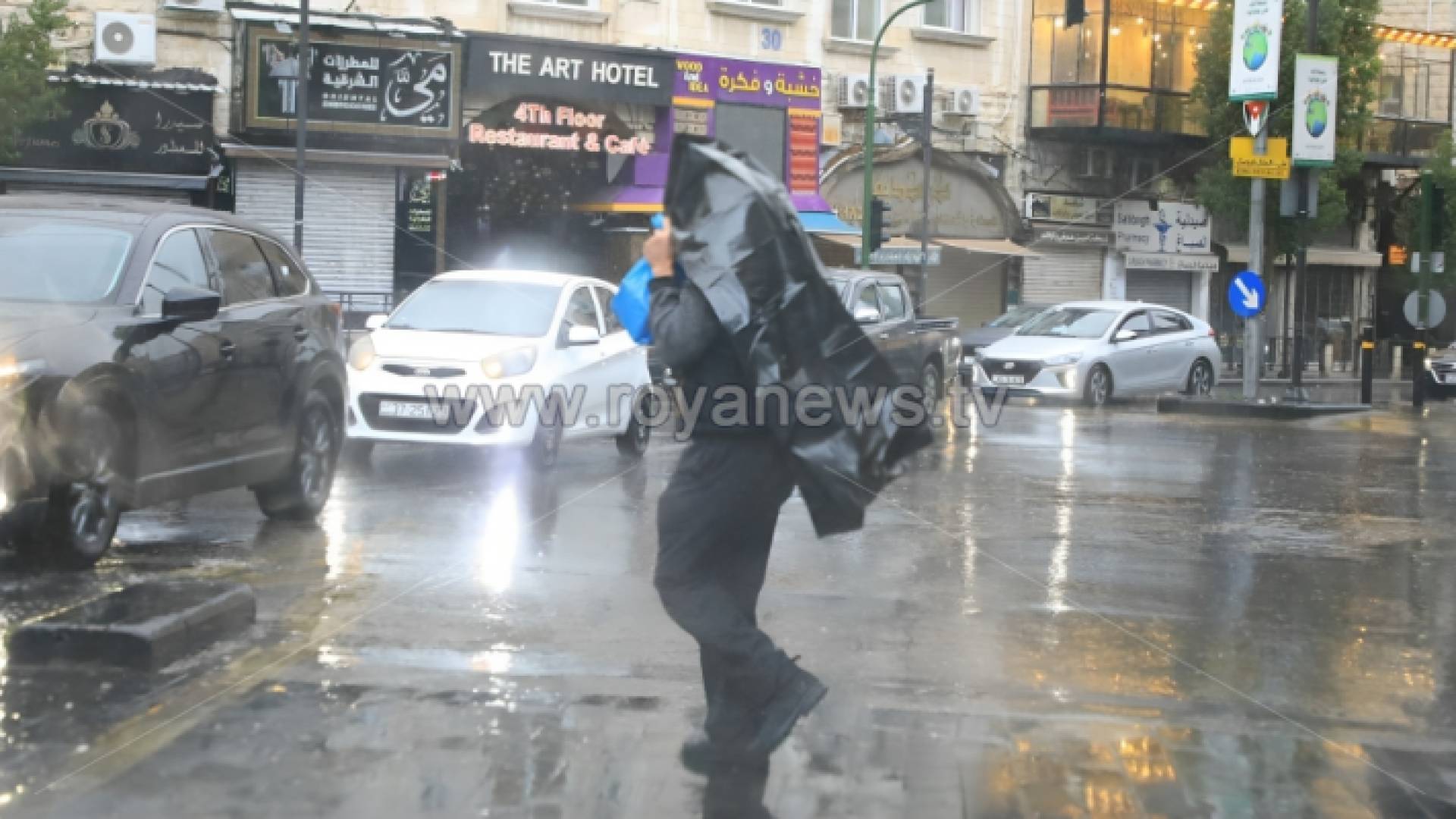 شخص يخطي جسده بعطف وسط هطول الأمطار في عمان