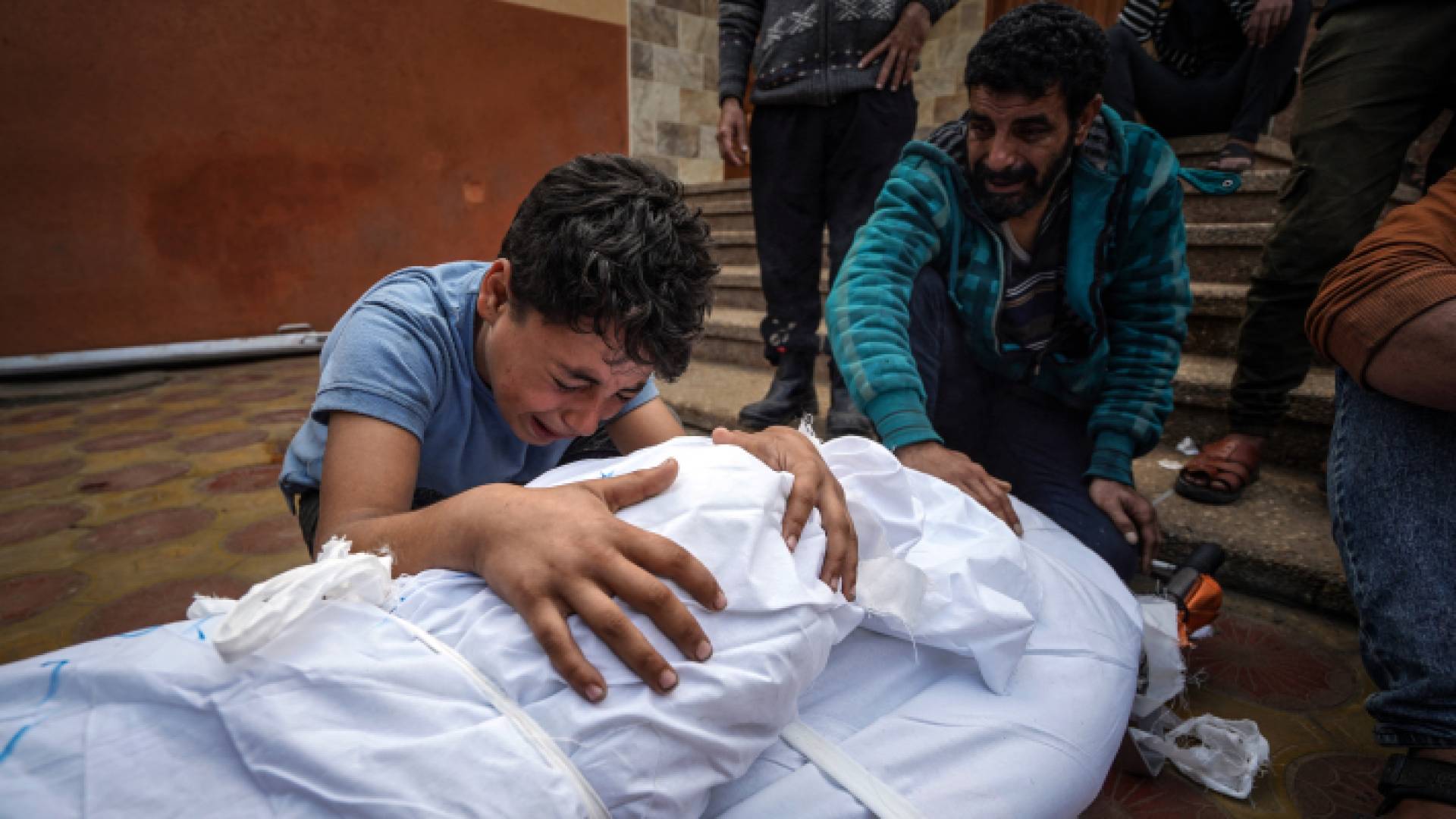 فتى فلسطيني يبكي بجانب جثمان والدته بعد استشهادها بغارة للاحتلال في قطاع غزة