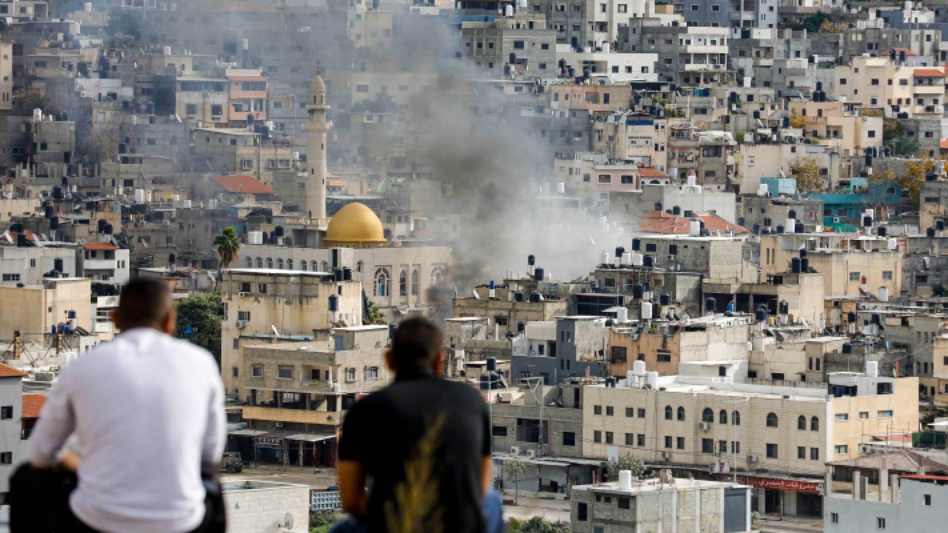 فلسطينيان يراقبان تصاعد الدخان خلال مواجهات اندلعت بين مقاومين وقوات الاحتلال بمخيم نور شمس في طولكرم