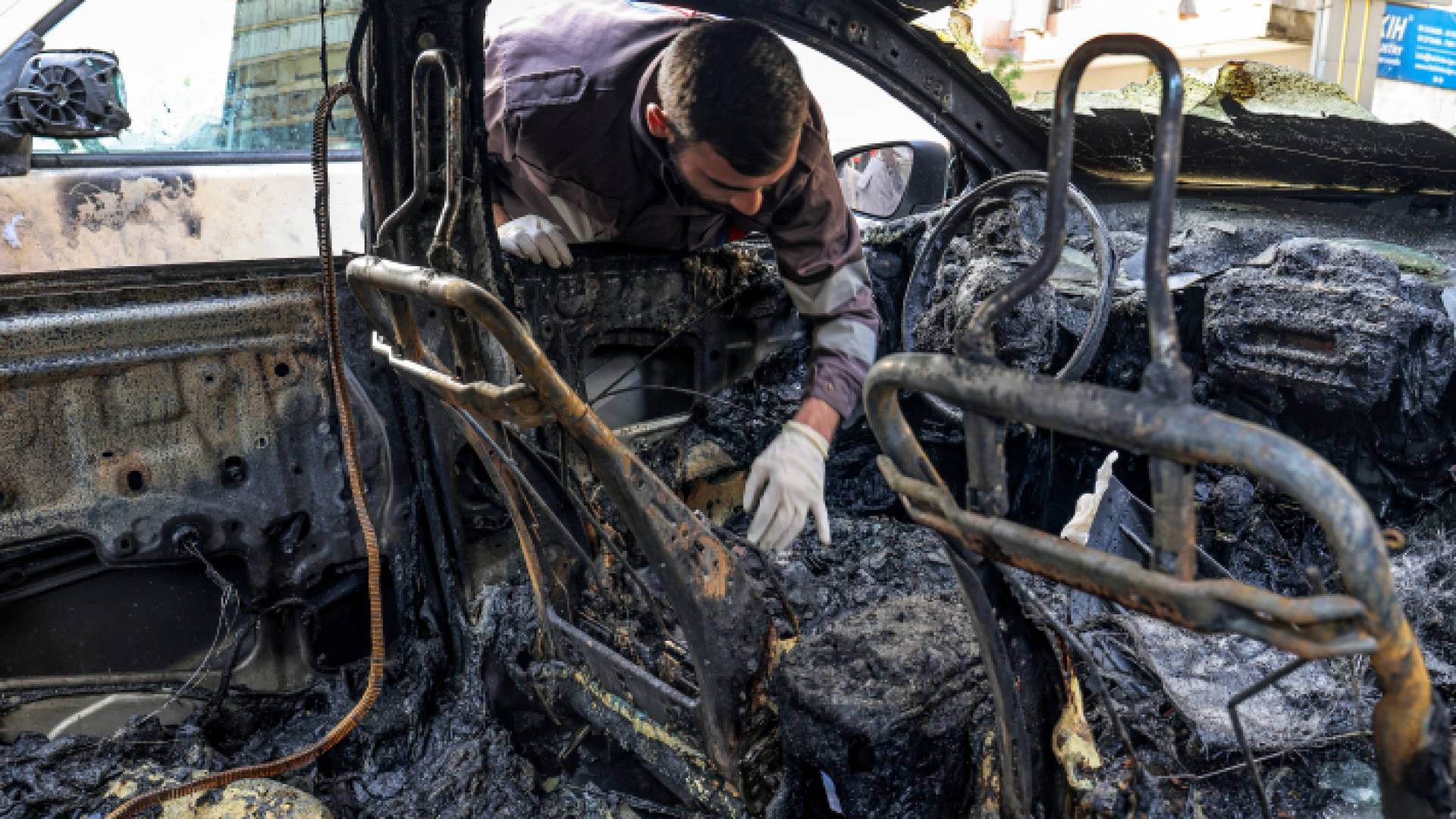 أحد رجال الدفاع المدني اللبناني يتفقد مركبة تضررت جراء عدوان الاحتلال - AFP