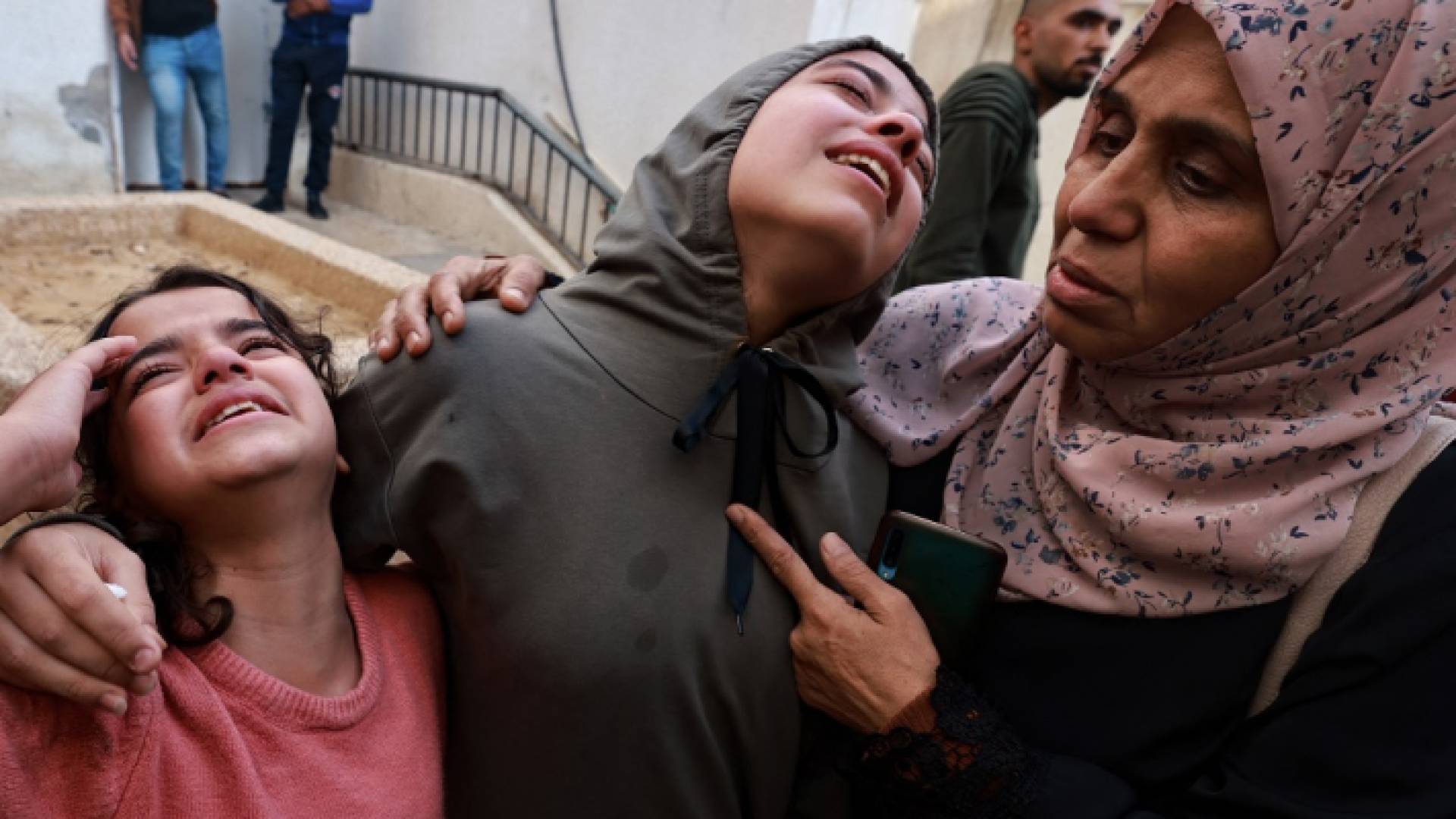 فلسطينية تحتضن ابنتيها اللتين تجهشان في البكاء بقطاع غزة