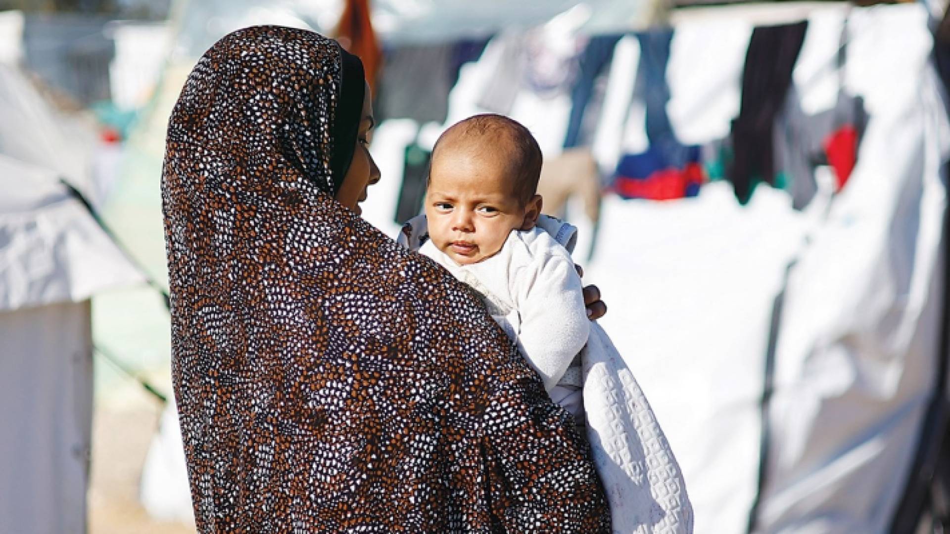 أم فلسطينية تحمل طفلها بين الخيام