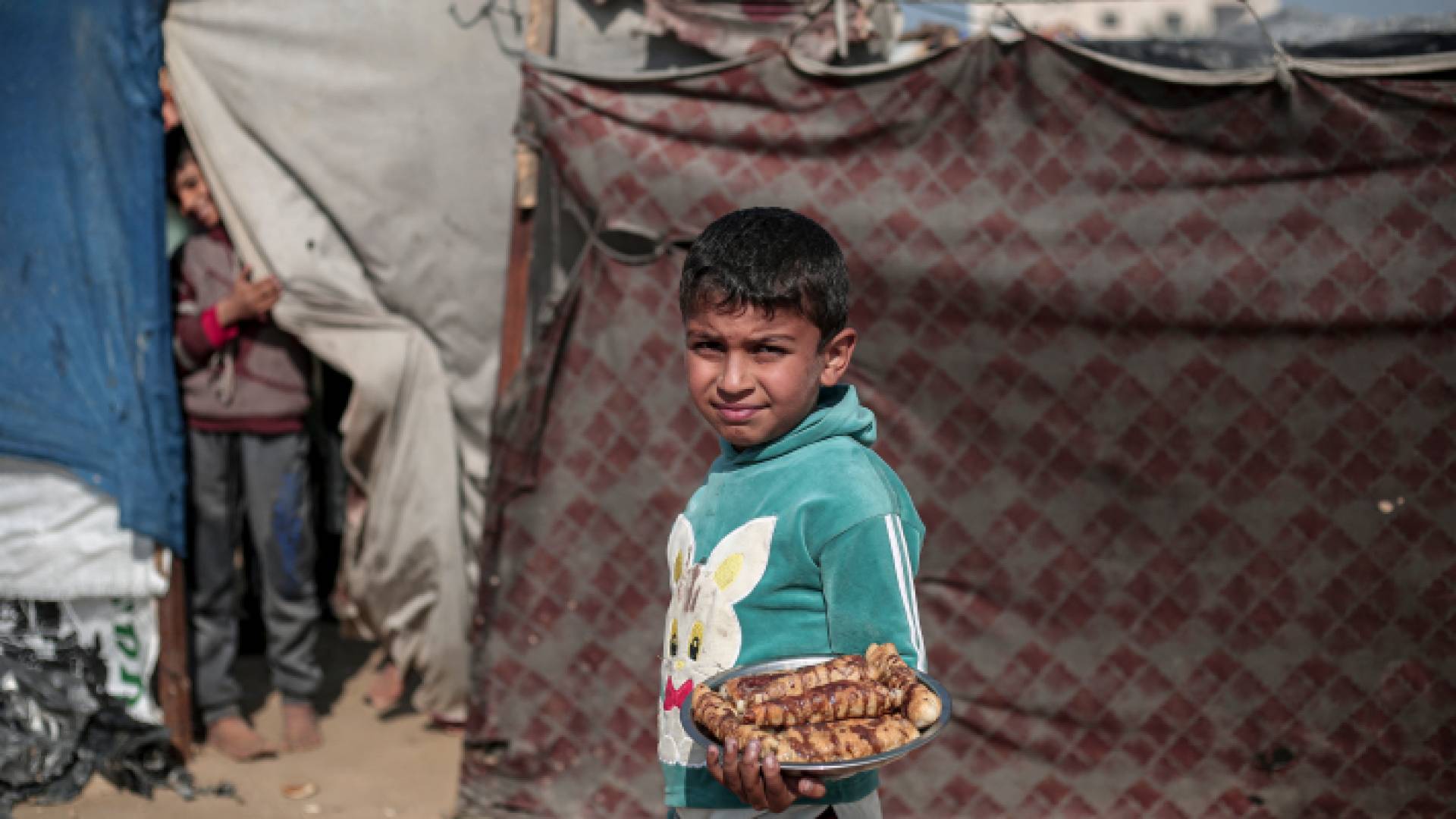 طفل فلسطيني نازح يحمل الحلوى بجوار ملاجئ مؤقتة في رفح