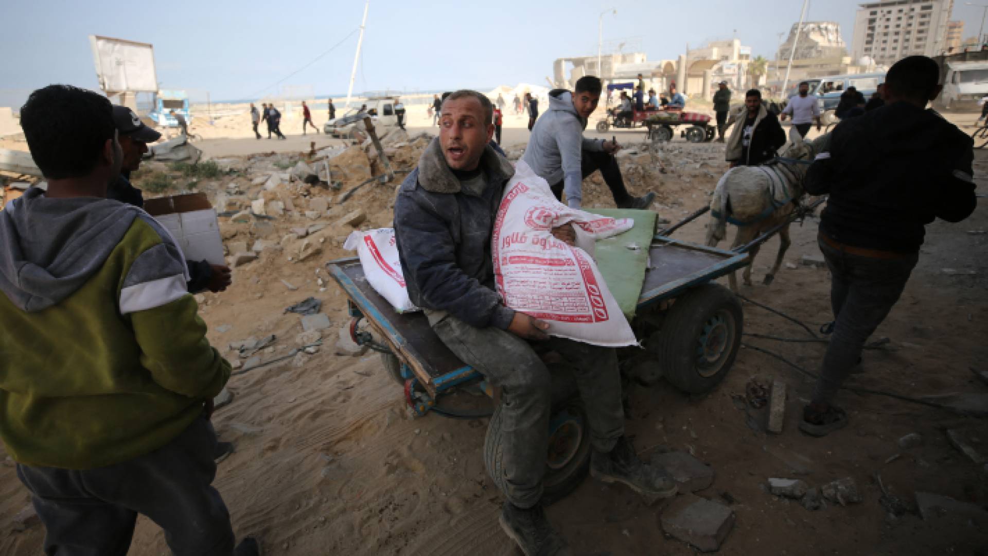 فلسطينيون ينقلون أكياس طحين مع وصول المساعدات الإنسانية إلى مدينة غزة - AFP