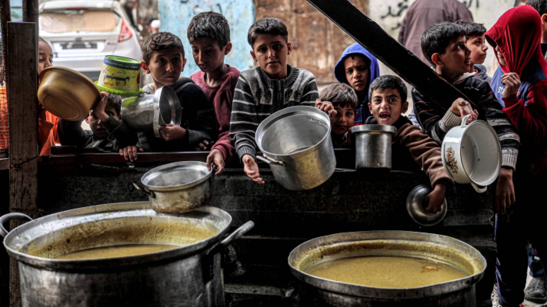 أطفال ينتظرون وهم يحملون أوانيا فارغة يصطفون للحصول على وجبات مقدمة من منظمة خيرية