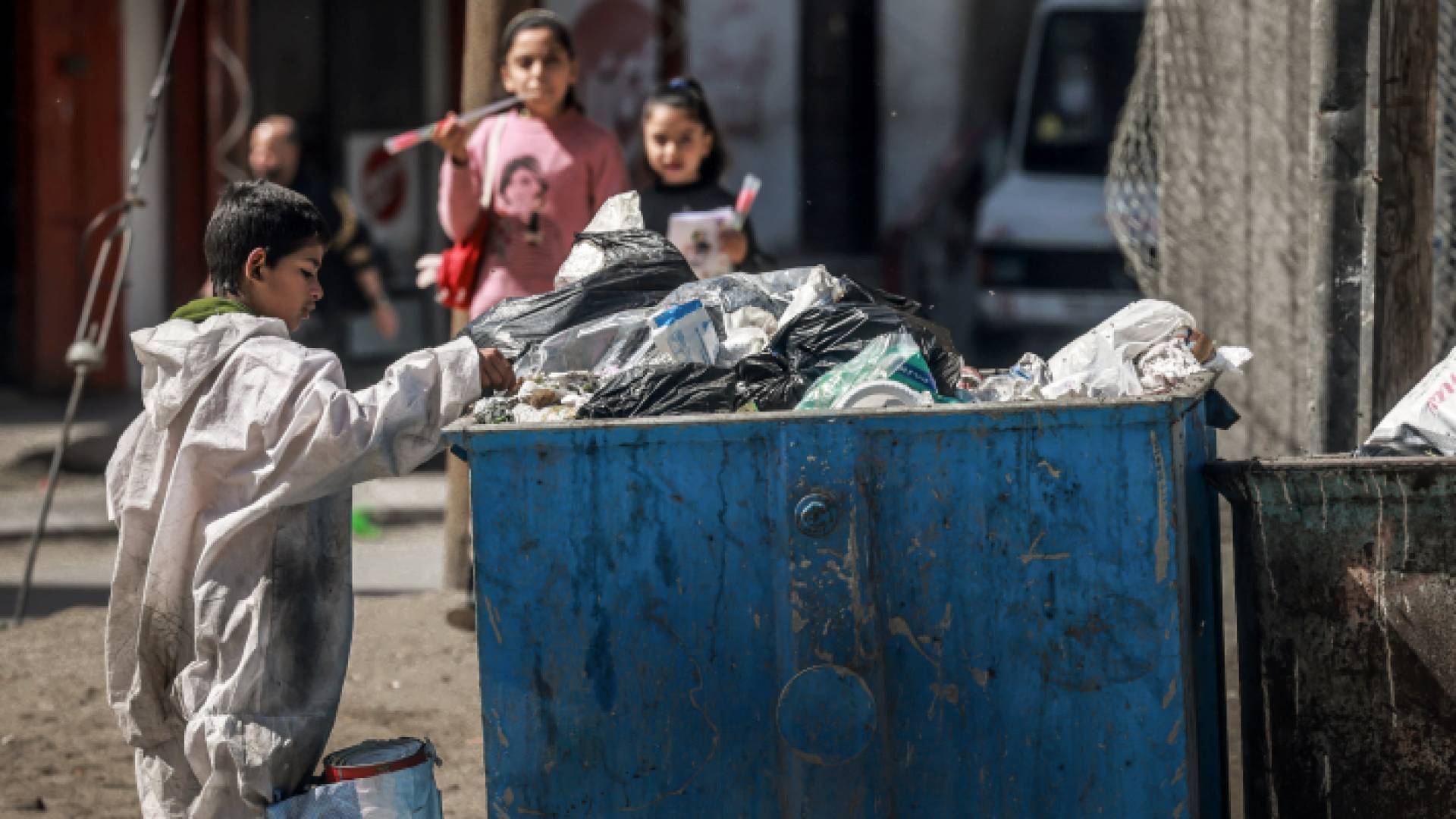 طفل فلسطيني يبحث في سلة نفايات عن طعام أو شي يستفيد منه