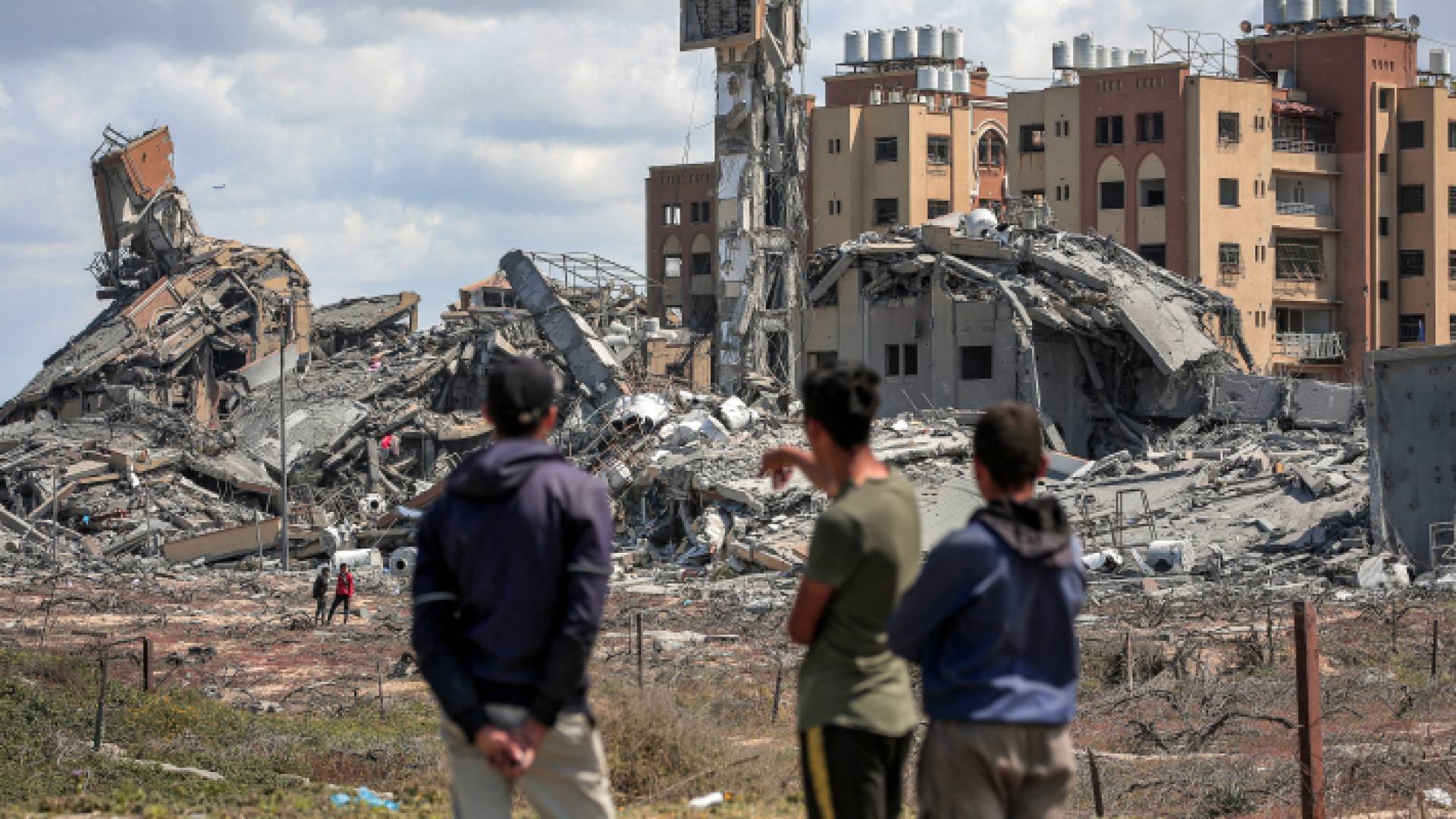 فلسطينيون ينظرون إلى ركام بناية هدمها الاحتلال الإسرائيلي في قطاع غزة