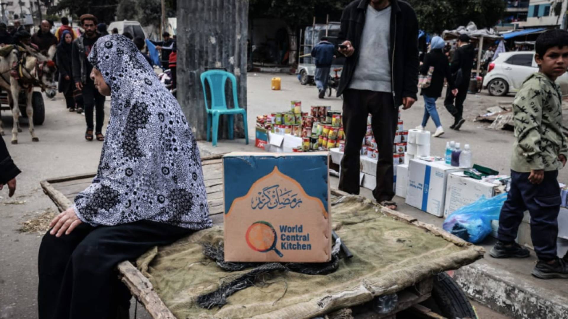 مسنة فلسطينية تجلس على عربة بجوار صندوق مساعدات