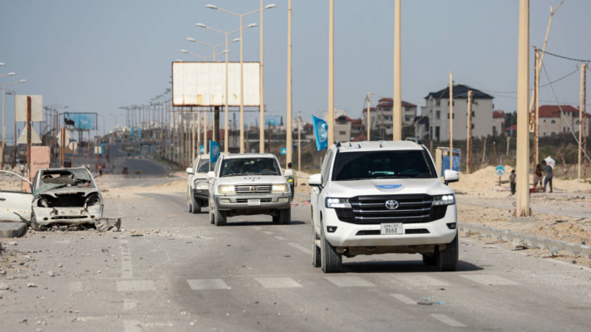 مركبات تابعة للأمم المتحدة تمر أمام سيارة مدمرة على طريق في مدينة غزة