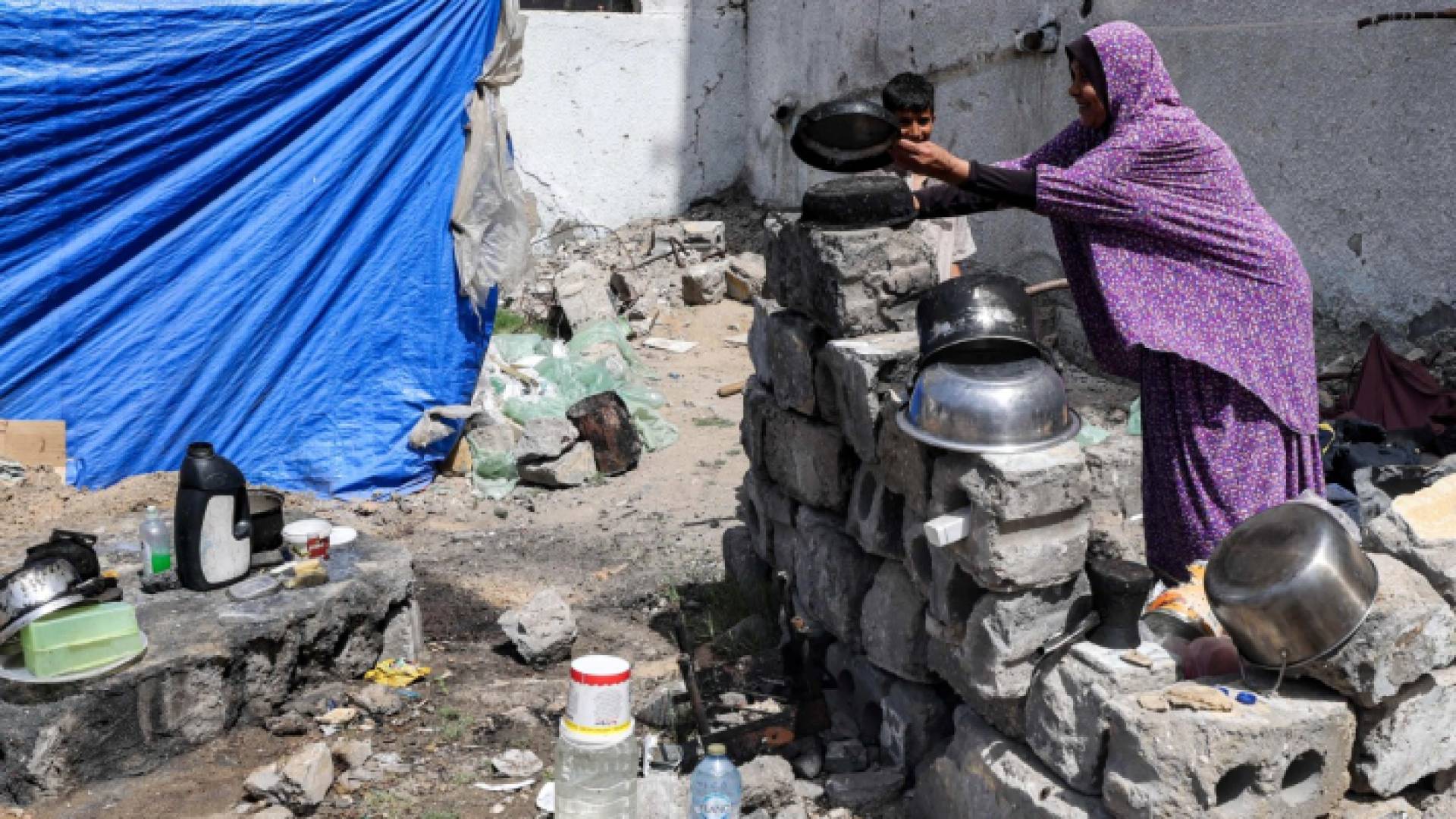 امرأة تغسل الأواني خارج خيمة نصبت بجوار مبنى مدمر في رفح جنوبي قطاع غزة - AFP
