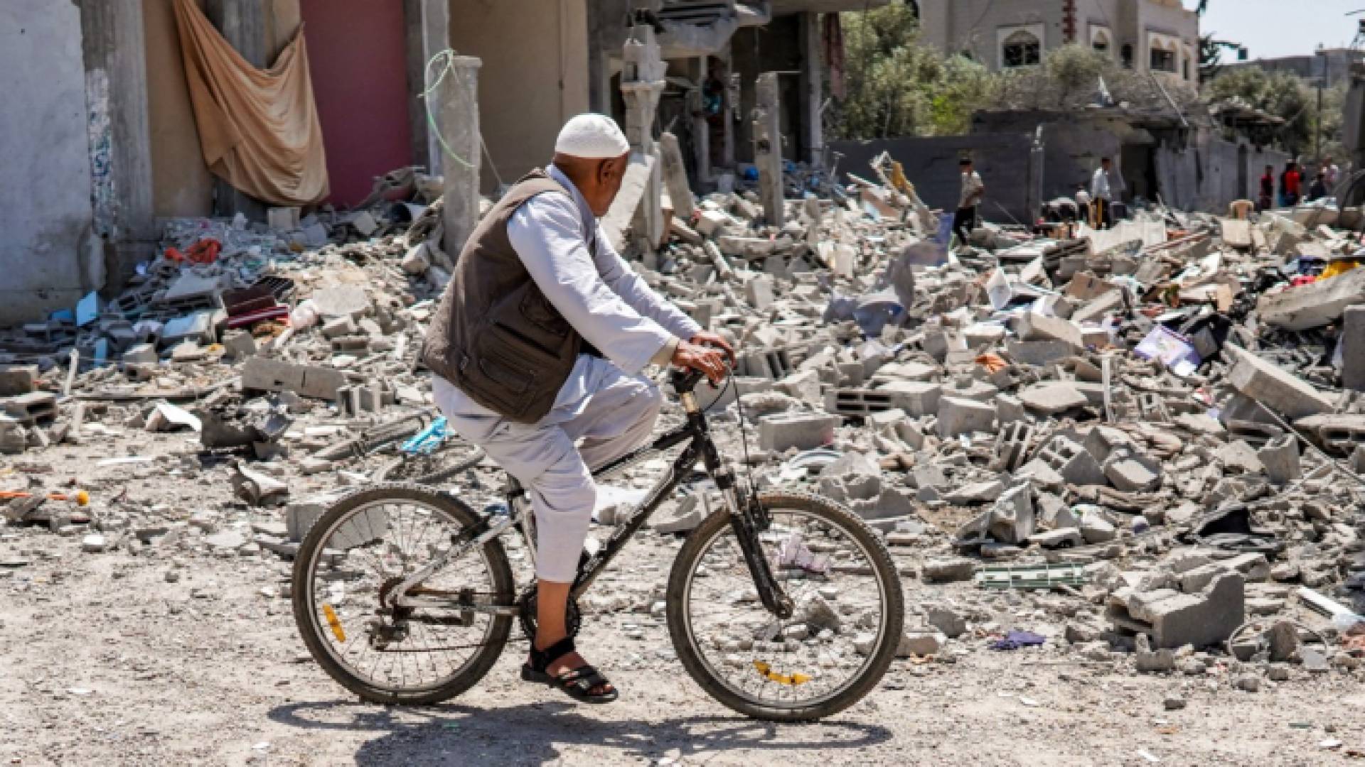 رجل يسير عبر دراجته الهوائية وسط حطام المنازل