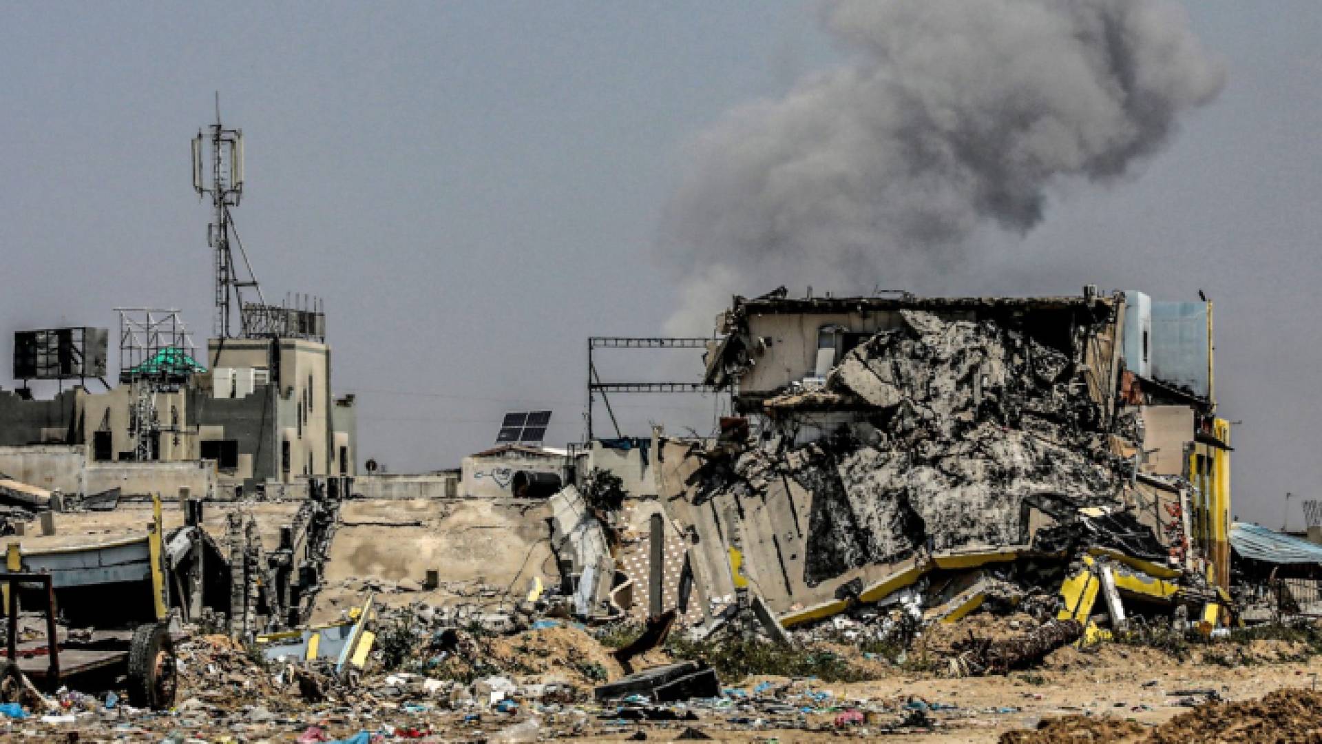 عمود من الدخان يتصاعد خلف مبنى منهار في مخيم المغازي للاجئين الفلسطينيين وسط قطاع غزة