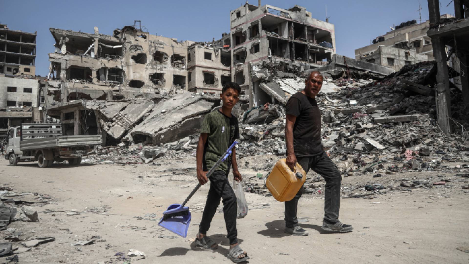 فلسطينيان يسيران وسط مبان دمرها الاحتلال خلال عدوانه على غزة - AFP