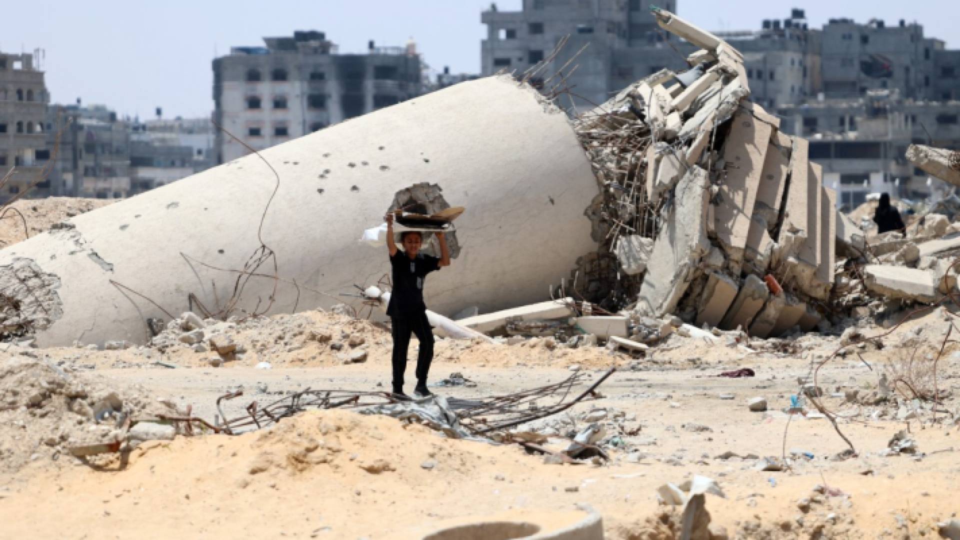 طفل فلسطيني ينقل قطعًا من الخشب ويسير بجوار مبنى دمره قصف الاحتلال في مدينة غزة