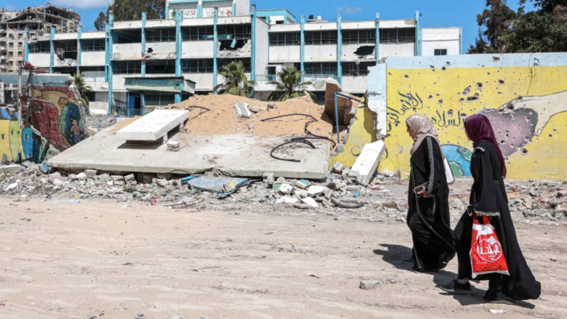 سيدتان فلسطينيتان بجانب مدرسة تديرها الأونروا في غزة دمرها الاحتلال