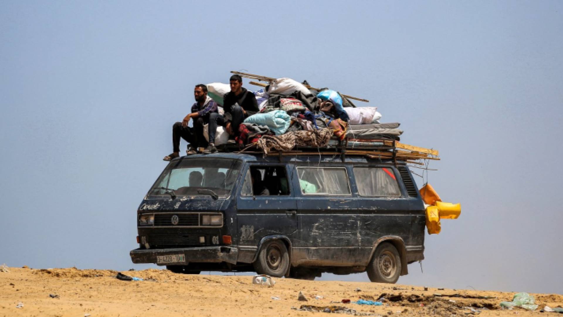 رجلان يركبان فوق حافلة محملة بالمراتب والأغطية وأشياء أخرى أثناء عودتهما إلى خان يونس جنوبي قطاع غزة