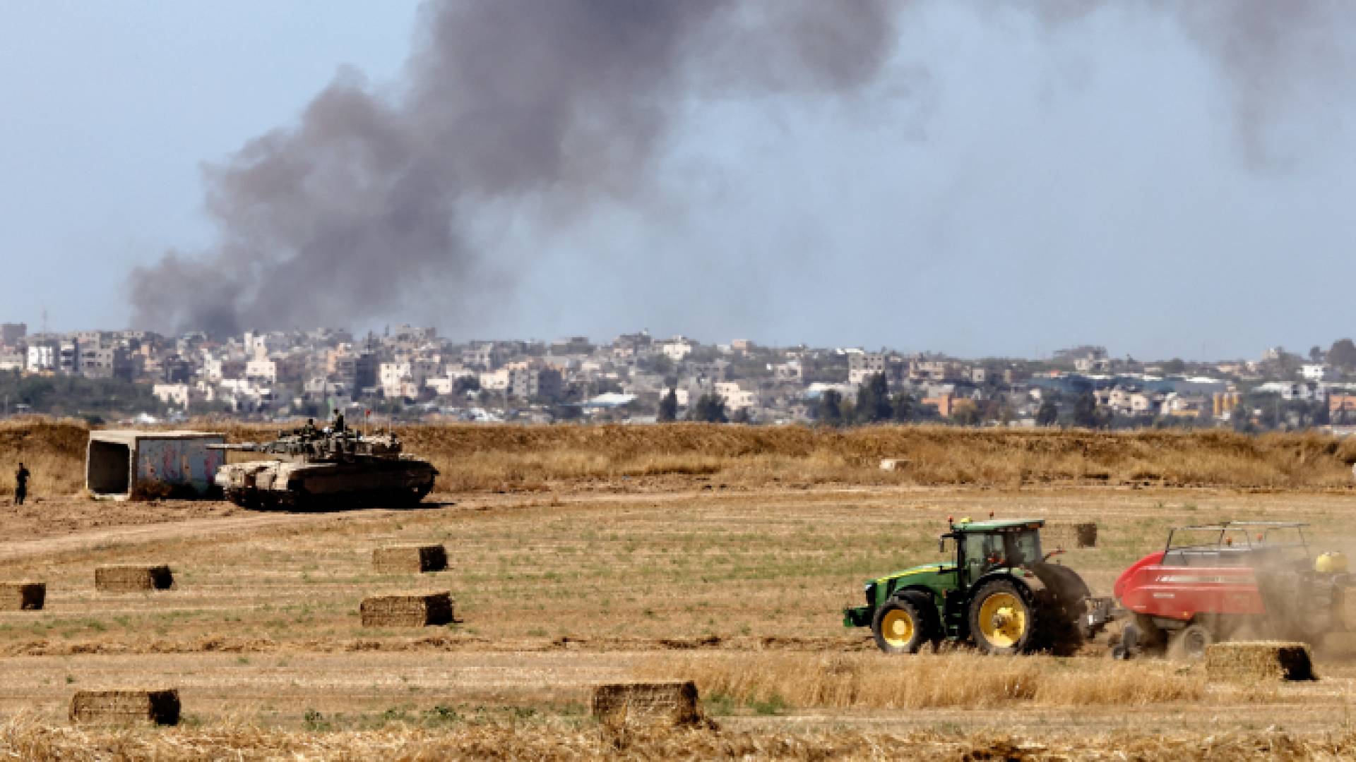 مركبة زراعية تحصد التبن أمام دبابة تابعة للجيش على حدود غزة