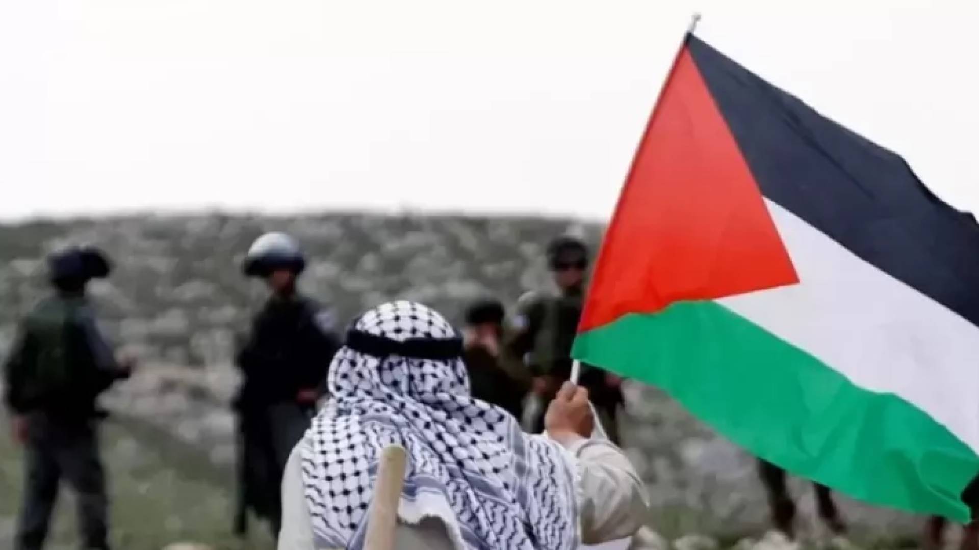 رجل مسن يحمل علم فلسطين أمام جنود الاحتلال