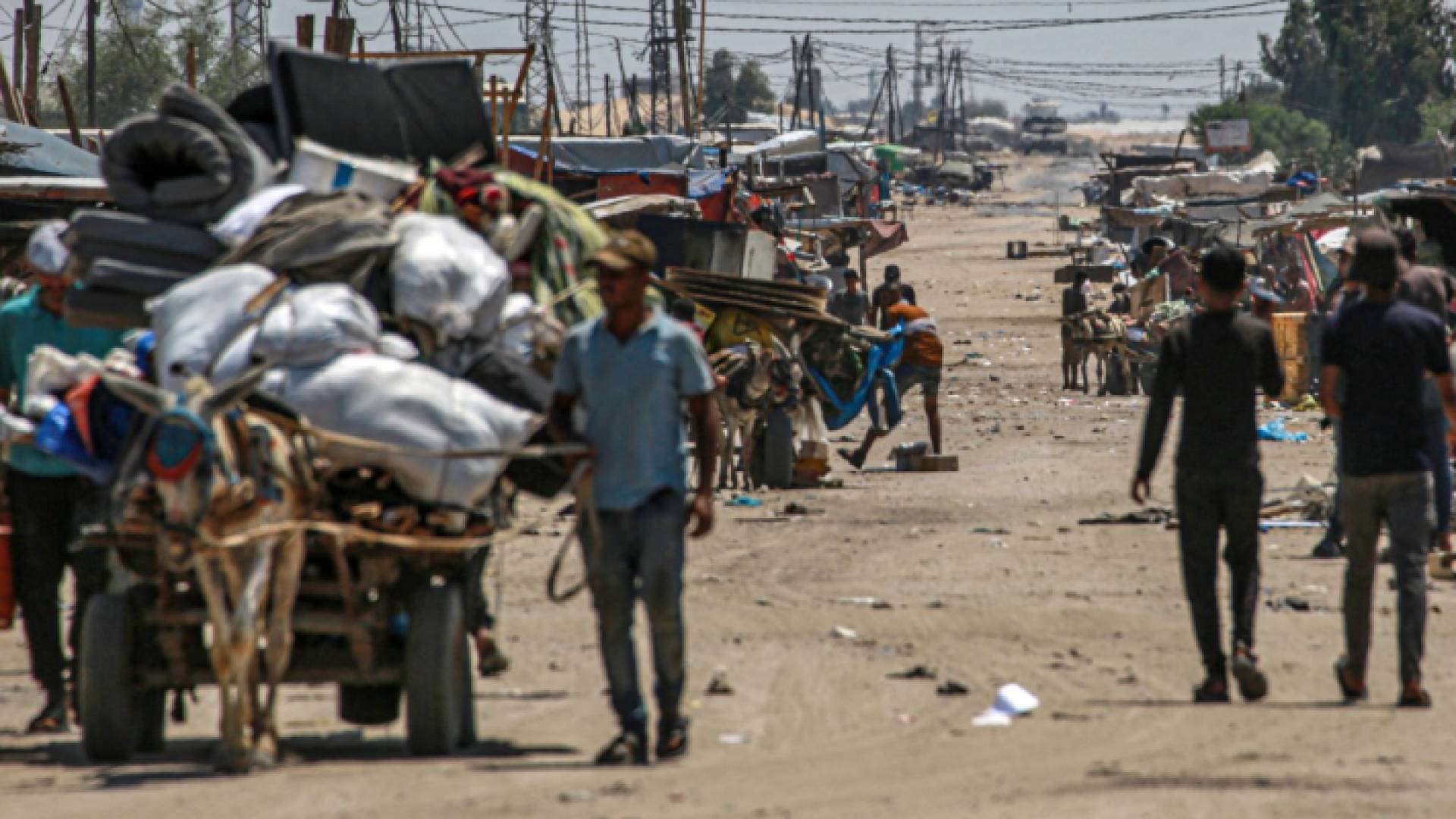 تقف دبابة "إسرائيلية" في الخلفية بينما يقوم الفلسطينيون النازحون بإخلاء منطقة شاكوش في رفح