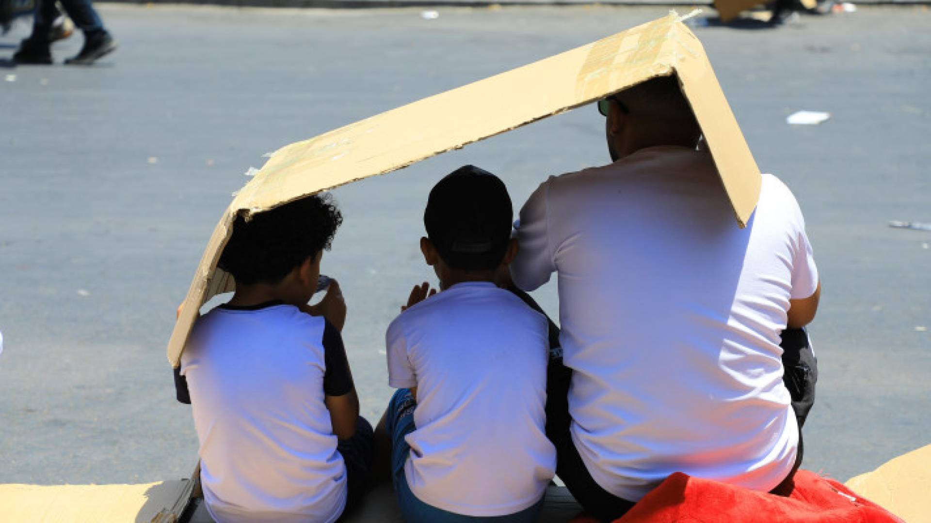 شخص وفتيان يستظلون بـ"كرتونة" من أشعة الشمس