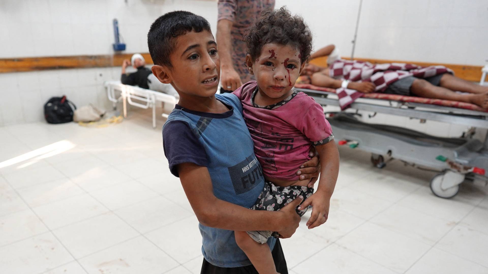 صبي يحمل شقيقه المصاب في مستشفى ناصر