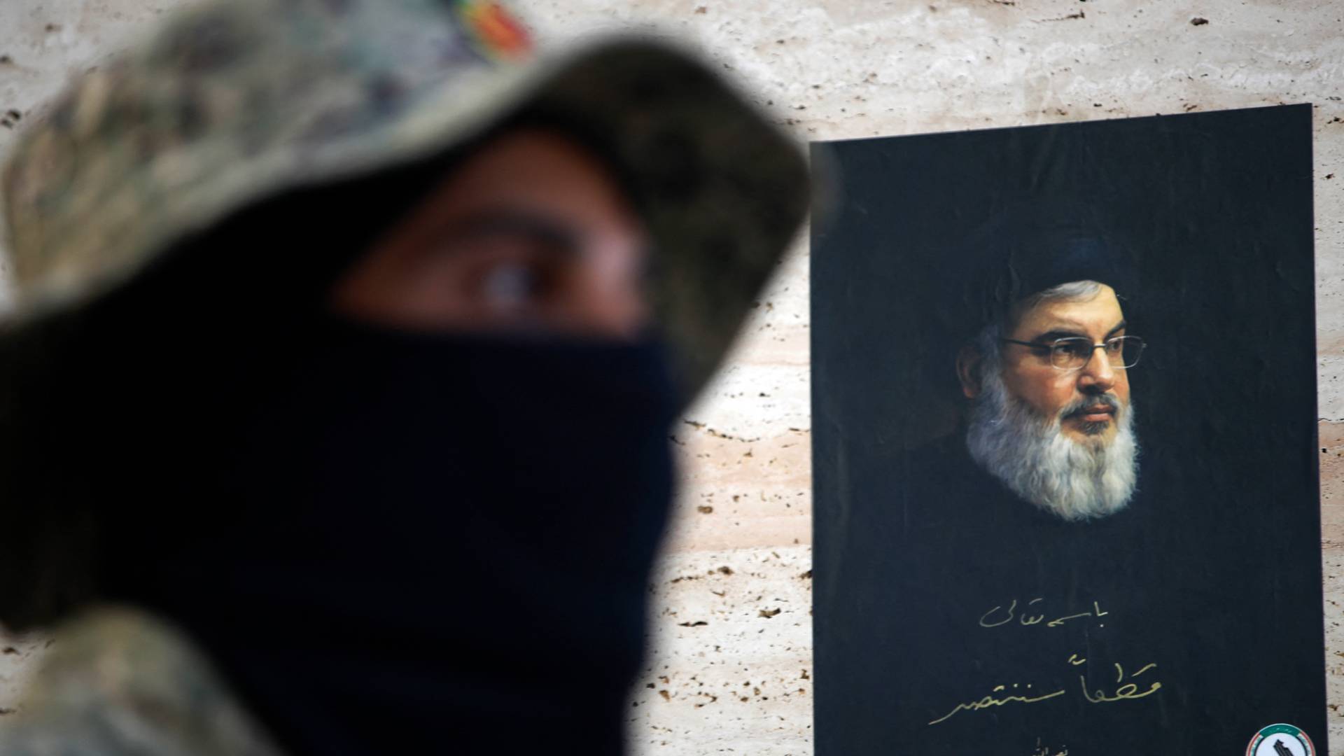 مقاتل عراقي ملثم يسير أمام ملصق للأمين العام لحزب الله حسن نصر الله