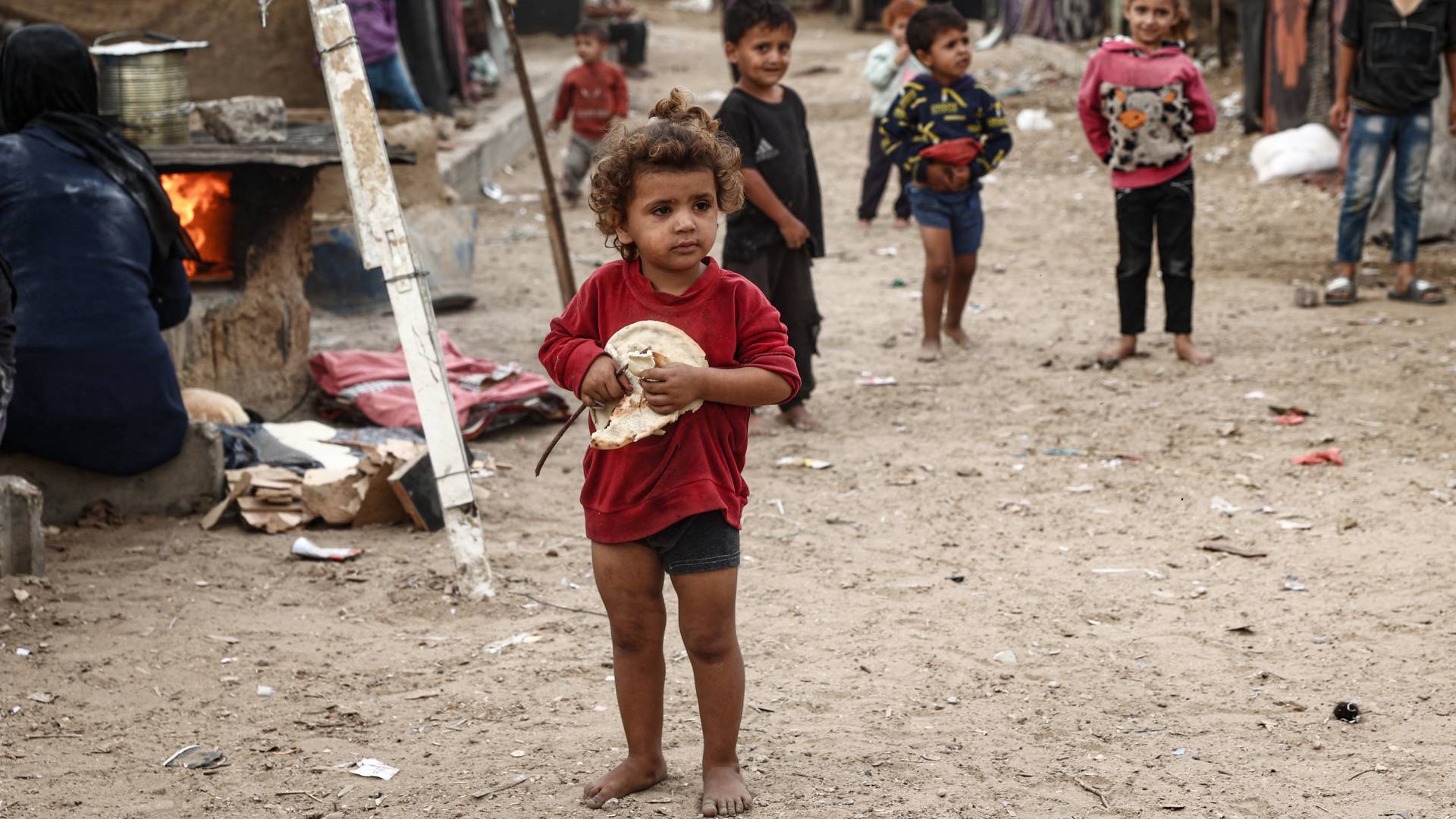 Tتاة فلسطينية تحمل رغيف خبز طازج في مخيم مؤقت للنازحين في دير البلح وسط قطاع غزة