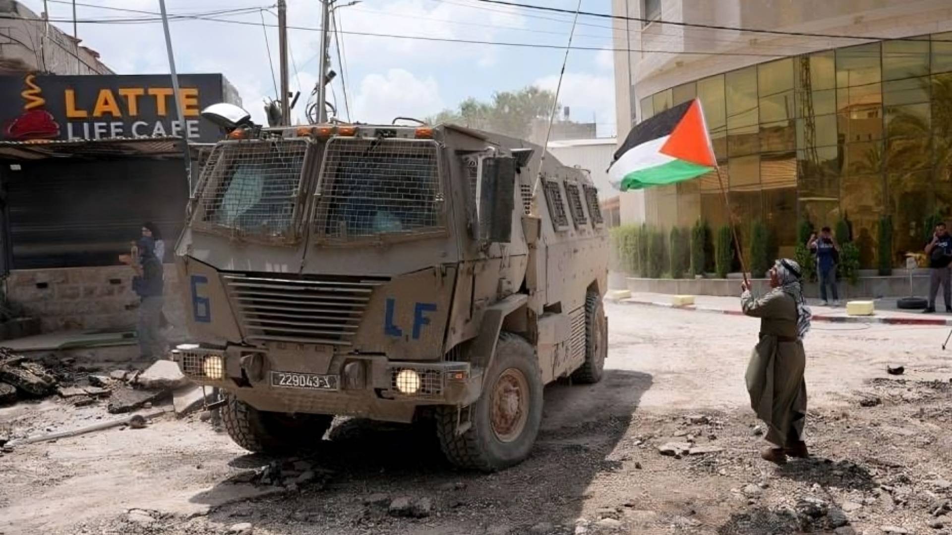 فلسطيني يرفع علم بلاده أمام جيش الاحتلال