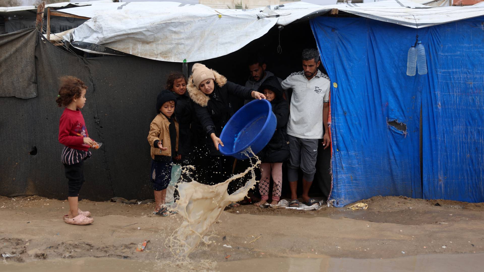 امرأة فلسطينية نازحة ترمي الماء أمام خيمة، بعد هطول أمطار غزيرة شمال دير البلح في وسط قطاع غزة