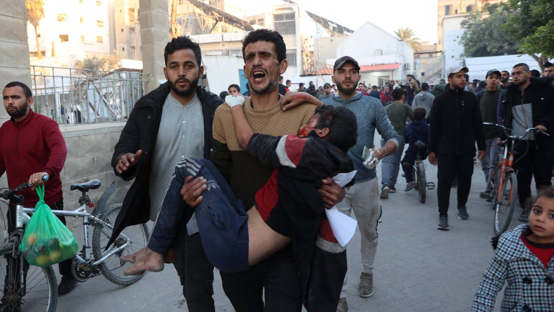 رجل فلسطيني يحمل طفلا مصابا بعد غارة للاحتلال على مدرسة في غزة