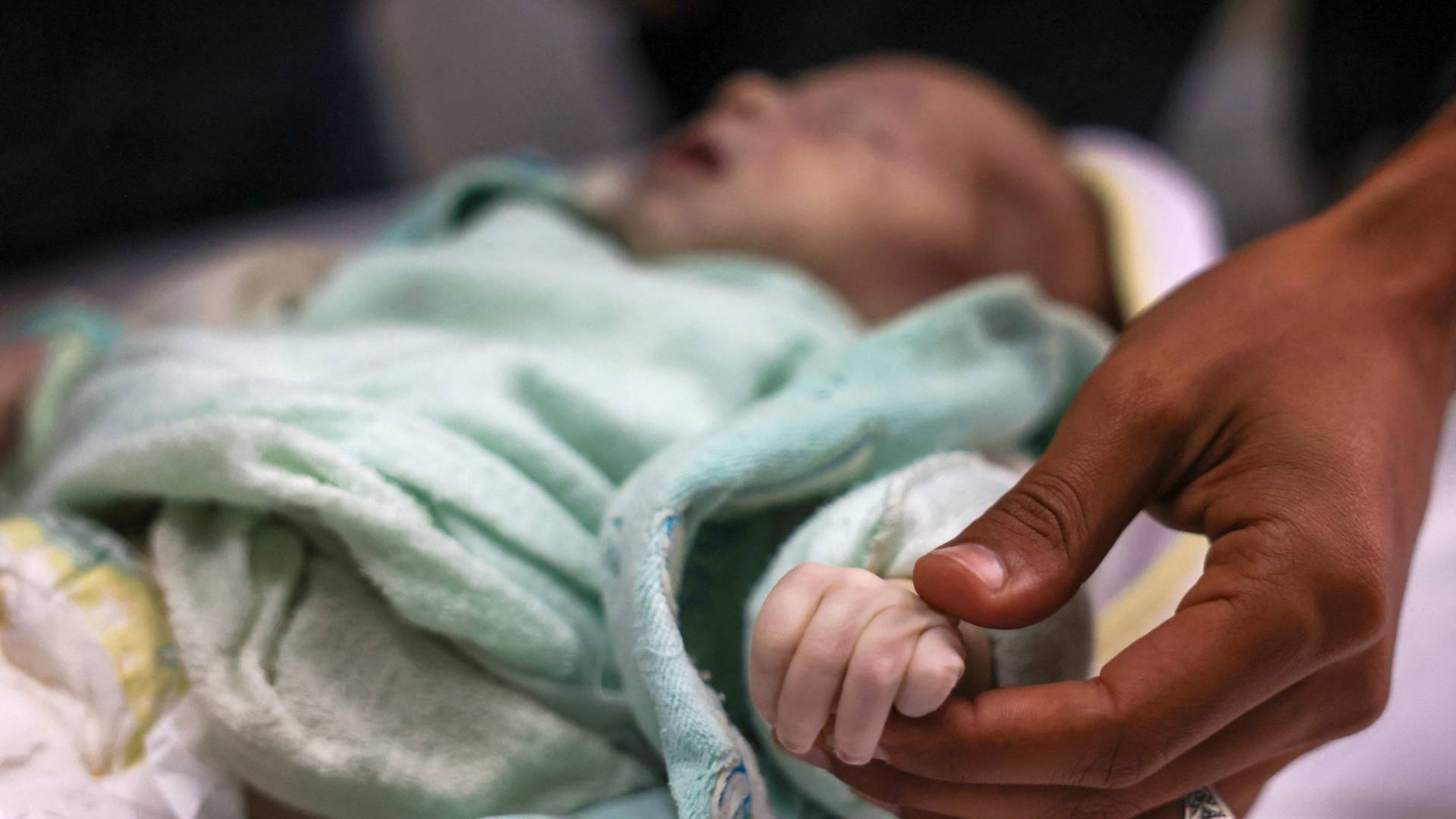 رجل يمسك بيد ابنة أخته سيلا الفصيح البالغة من العمر ثلاثة أسابيع، والتي توفيت بسبب انخفاض حرارة الجسم