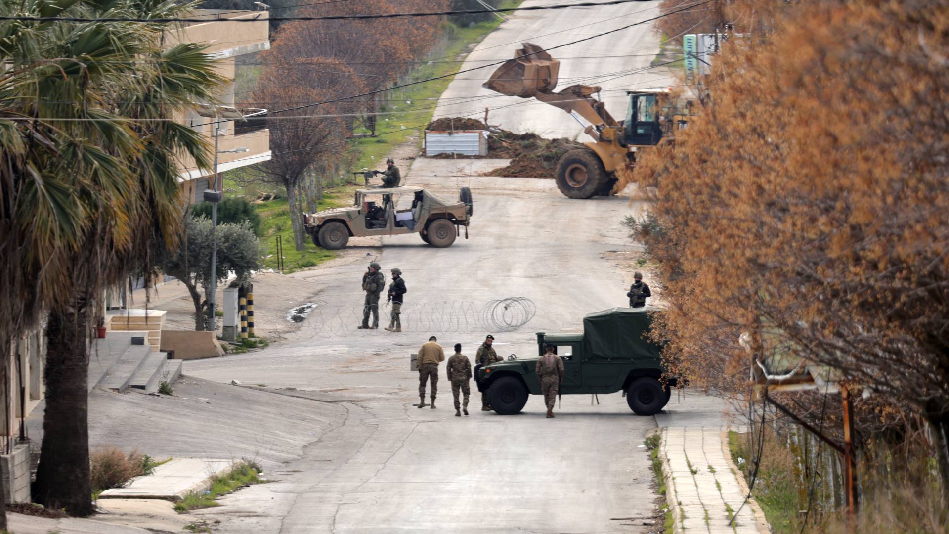 جنود من الجيش اللبناني (يمين) وقوات الاحتلال بالقرب من مركباتهم على جانبي حاجز سلك شائك، جنوب لبنان