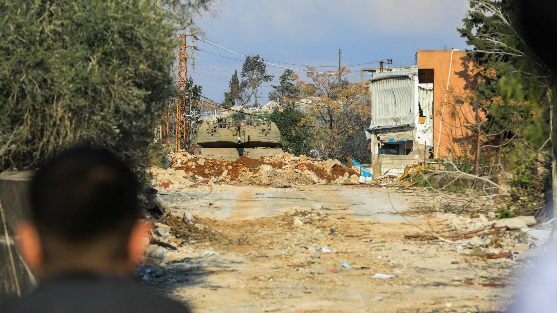 ينظر سكان لبنانيون إلى دبابة تابعة لجيش الاحتلال الإسرائيلي تسد مدخل قريتهم الجنوبية حولا